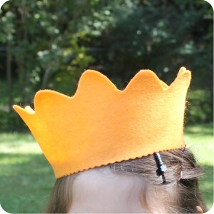 May include: A bright orange felt crown with a scalloped edge. The crown is worn on a person's head.