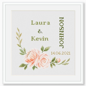May include: A white cross-stitch embroidery with a floral design featuring two pink roses and green leaves. The text "Laura & Kevin JOHNSON 14.06.2021" is embroidered in green and gold.