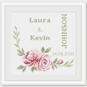 May include: Cross-stitch embroidery featuring a floral design with two pink roses and green leaves. The text "Laura & Kevin JOHNSON 14.06.2021" is stitched in the centre.