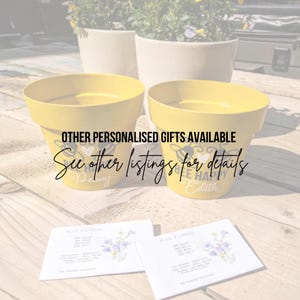 May include: Two yellow ceramic flower pots with bee-themed designs and personalised names "Penny" and "Edith". The pots are sitting on a wooden surface with wildflower seed packets.