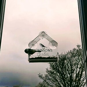 May include: A clear plastic bird feeder with suction cups attached to a window. The feeder has a small bird silhouette and the text "The Johnson's Garden" printed on it.
