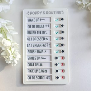 May include: A white plastic chart with a checklist for a child's daily routine. The chart is titled "POPPY S ROUTINE." and includes tasks such as "Wake Up", "Go to Toilet", "Brush Teeth", "Get Dressed", "Eat Breakfast", "Brush Hair", "Shoes On", "Coat On", "Pick Up Bag", and "Go to School". Each task has a checkbox with a green tick or a red X.
