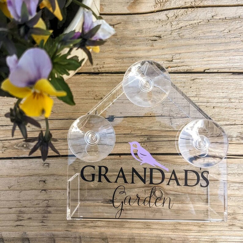 May include: A clear acrylic bird feeder with three suction cups. The feeder has a sign that says "Grandad's Garden" with a purple bird silhouette.
