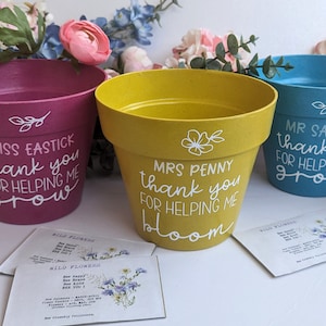 May include: Three colourful flower pots with personalised messages for teachers. The pink pot says "Miss Eastick thank you for helping me grow". The yellow pot says "Mrs Penny thank you for helping me bloom". The blue pot says "Mr Sayers thank you for helping me grow".