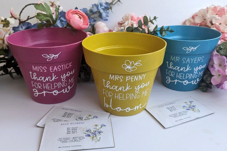 May include: Three colorful flower pots with personalized messages for teachers. The pink pot says "Miss Eastick thank you for helping me grow". The yellow pot says "Mrs Penny thank you for helping me bloom". The blue pot says "Mr Sayers thank you for helping me grow".
