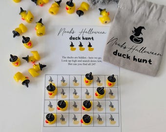 May include: A Halloween-themed duck hunt game. The game includes yellow duck figurines wearing black witch hats, a game board, and a small gray bag. The game board has a grid with numbers and duck illustrations. The text on the game says "Noah's Halloween duck hunt" and "Happy Halloween."