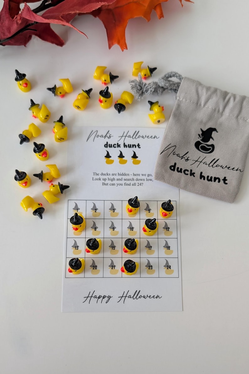 May include: A Halloween-themed duck hunt game. The game includes yellow duck figurines wearing black witch hats, a game board, and a small gray bag. The game board has a grid with numbers and duck illustrations. The text on the game says "Noah's Halloween duck hunt" and "Happy Halloween."