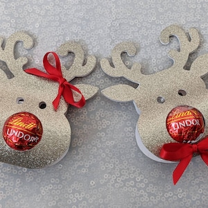 May include: Two silver glitter reindeer head ornaments with red bows and Lindor chocolate truffles in their mouths.