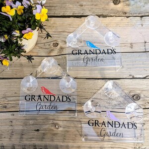 May include: Three clear acrylic bird feeders with suction cups. Each feeder has the text "Grandad's Garden" and a different coloured bird silhouette. The feeders are on a wooden surface.