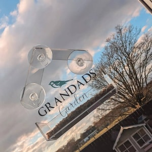 May include: A clear acrylic bird feeder with suction cups for attaching to a window. The feeder has a small bird silhouette and the text "Grandads Garden".