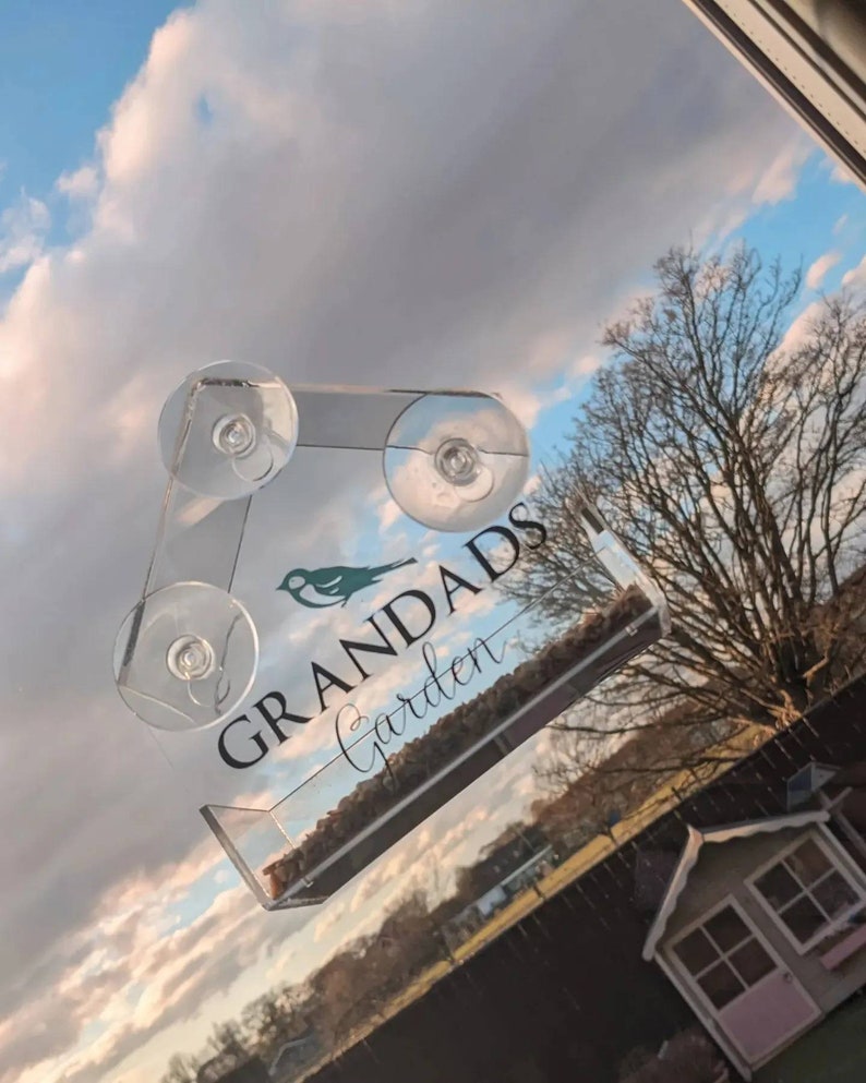 May include: A clear acrylic bird feeder with suction cups for attaching to a window. The feeder has a small bird silhouette and the text "Grandads Garden".