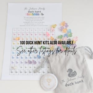 May include: A printed game sheet with a grid and the text "The Johnson Family duck hunt". Includes a small drawstring bag, a button, and colorful duck-shaped game pieces. The text "100 DUCK HUNT KITS ALSO AVAILABLE" is also visible.