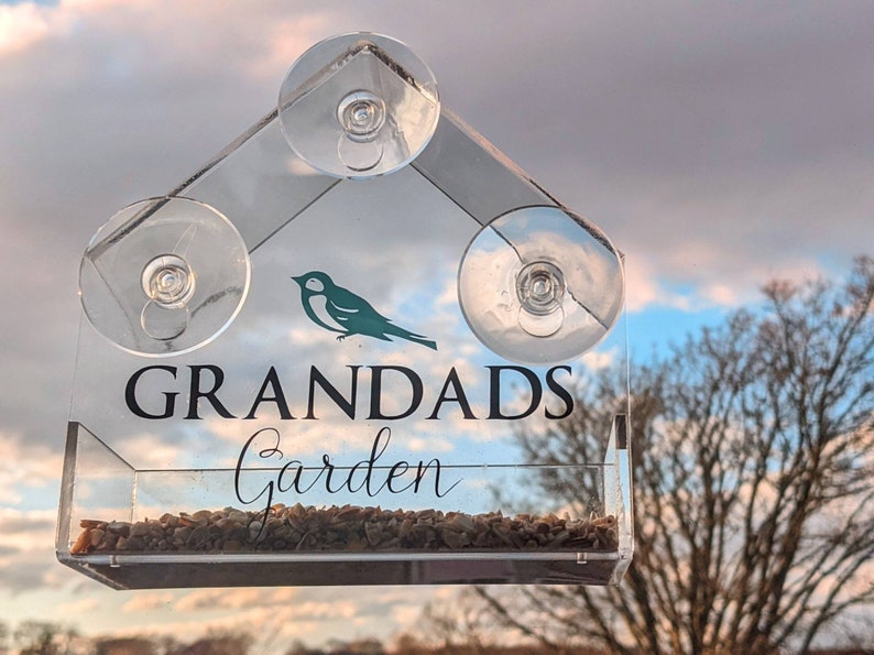 May include: A clear acrylic bird feeder with suction cups, designed to attach to a window. The feeder has a small bird silhouette and the text "Grandads Garden".
