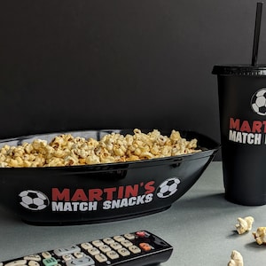 以下が含まれることがあります： サッカーボールのグラフィックと「MARTIN'S MATCH SNACKS」の文字が書かれた黒いボウルにポップコーンが入っています。サッカーボールのグラフィックと「MARTIN'S MATCH DRINK」の文字が書かれた黒いカップにストローが刺さっています。