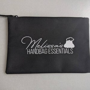 May include: Black zippered pouch with white text that reads "Melissa's Handbag Essentials" and a white silhouette of a handbag.