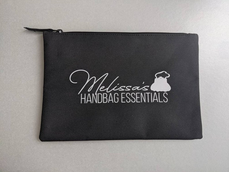 May include: Black zippered pouch with white text that reads "Melissa's Handbag Essentials" and a white silhouette of a handbag.
