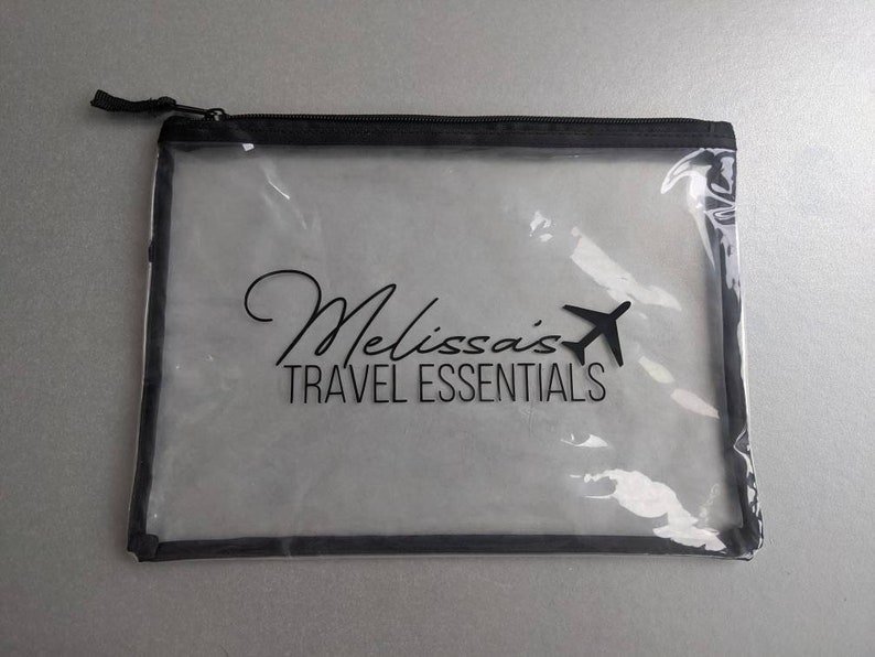 May include: Clear plastic travel pouch with a black zipper and black trim. The pouch has the text "Melissa's Travel Essentials" printed on it.