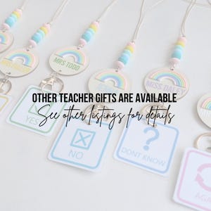 May include: A set of rainbow-themed teacher gifts with personalized name tags. The gifts include a lanyard with colorful beads and a wooden rainbow charm. The image also shows a set of four keychains with different designs, including a checkmark, an X, a question mark, and a circle with an arrow. The text "OTHER TEACHER GIFTS ARE AVAILABLE See other listings for details" is visible in the image.