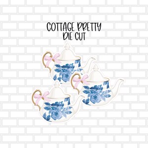 May include: Three blue and white teapots with pink bows. The teapots have a floral design and are on a white brick background. The text "Cottage Pretty Die Cut" is above the teapots.
