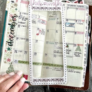Op de afbeelding: Een transparante maandelijkse planner overlay van plastic met een witte rand en een roze titel "Deze maand". De overlay is geplaatst over een december-kalenderpagina met handgeschreven notities en stickers.