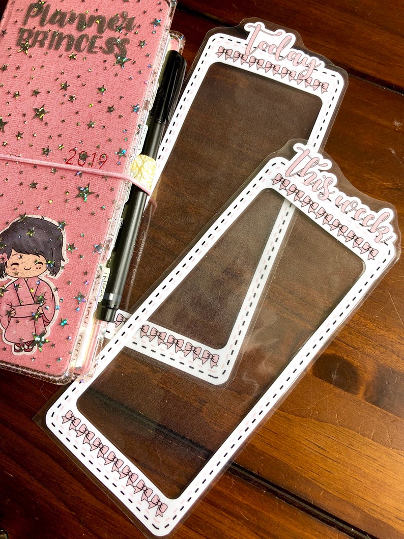 Op de afbeelding: Twee transparante plastic planner-bladwijzers met roze strikken en witte gestippelde lijnen. De bovenste bladwijzer zegt "Vandaag" en de onderste bladwijzer zegt "Deze week".