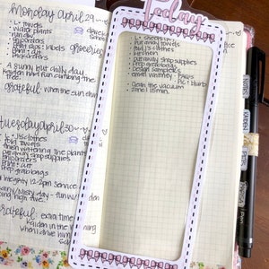 Op de afbeelding: Een close-up van een roze en witte planner met een doorzichtig plastic vel met het woord "Vandaag" erop. Het vel heeft een roze en wit strikdesign rond de randen. De planner heeft een rasterpatroon en is gevuld met handgeschreven notities.