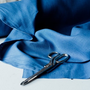 May include: A pair of silver scissors lying on a blue fabric background.