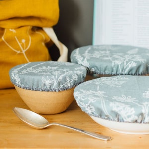 May include: Three ceramic bowls with floral patterned fabric covers. The bowls are on a wooden surface.