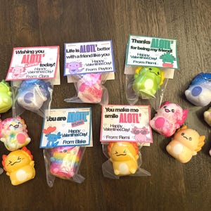 May include: A collection of colorful axolotl toys in clear plastic bags, each paired with a Valentine's Day card. The cards feature phrases like "Wishing you ALOTL love today!" and "You make me smile ALOTL!"