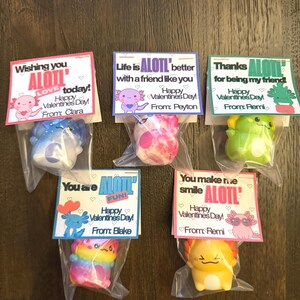 May include: Six Valentine's Day gifts featuring axolotl-themed toys in clear plastic bags. Each bag has a colorful card with a Valentine's Day message and the word "ALOTL". The axolotls are various colors, including blue, pink, green, rainbow, and yellow.