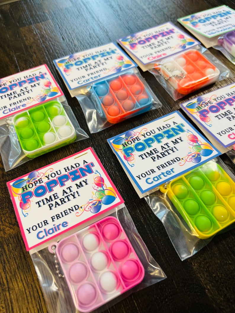 May include: A set of party favours featuring colourful pop-it fidget toys with a tag that says "Hope you had a poppin' time at my party!" with the name "Claire" or "Carter" on the tag.