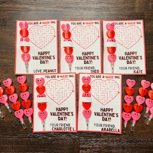 Op de afbeelding: Zes Valentijnsdagkaarten met een doolhof op elke kaart. Elke kaart heeft een roze hart met een smiley erop en een potlood met een roze hartgum. De kaarten zeggen "You are A-Maze-ing" en "Happy Valentine's Day!" met een gepersonaliseerd bericht voor elke ontvanger.
