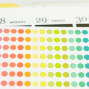 以下が含まれることがあります： 28日、29日、30日の日付が書かれたカレンダーのページ。各日付には、ピンクから始まり青に変わる色のドットが並んでいます。