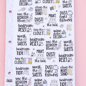 May include: A sheet of bedroom cleaning task stickers with various illustrations and text. The stickers include phrases like "wash the sheets," "dust light fixtures," and "tidy the closet." The background is a light pink color.