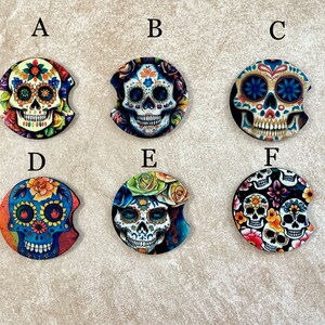 May include: Six round car coasters with a Day of the Dead theme. The coasters feature colorful sugar skulls with floral designs. The coasters are labeled A through F.