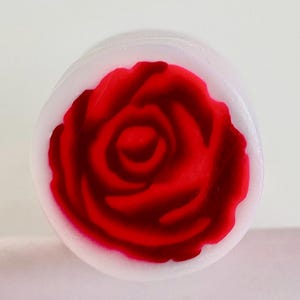 May include: A white round soap with a red rose design.