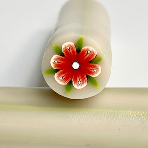 May include: A white polymer clay roller with a red flower design. The flower has white petals with red edges and a white center. The flower is surrounded by green leaves.