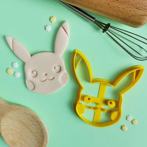 May include: Two cookie cutters in the shape of Pikachu, one is yellow and the other is white.