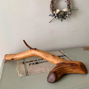 May include: A handcrafted wooden decorative branch with a natural finish, resting on a burlap cloth. The cloth has the text "LANCASTER FARMER" printed on it. A small wreath of twigs and dried flowers hangs on the wall in the background.