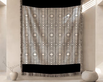 Könnte beinhalten: Eine schwarz-cremefarbene Decke mit einem geometrischen Muster aus vertikalen Linien und Rauten. Die Decke hat einen schwarzen Rand oben und unten und einen Fransenrand. Die Decke hängt an einer Wand.