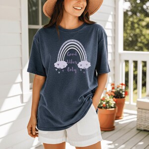 May include: Navy blue t-shirt with a rainbow graphic and the text "Good Vibes Only". The rainbow design features white, lavender, and gray colors. The shirt is paired with white shorts.