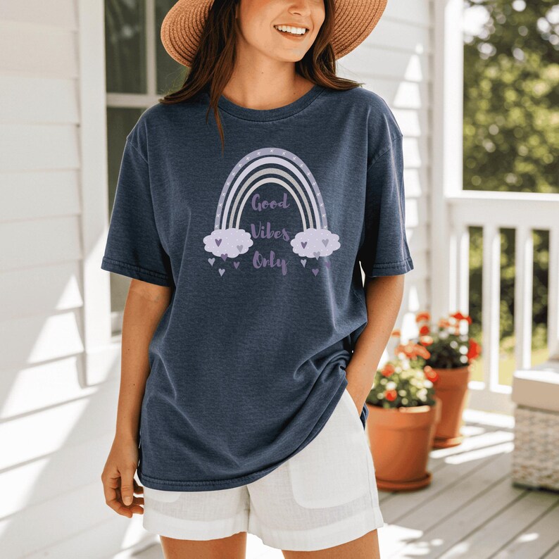 May include: Navy blue t-shirt with a rainbow graphic and the text "Good Vibes Only". The rainbow design features white, lavender, and gray colors. The shirt is paired with white shorts.