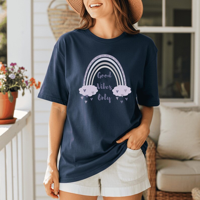 May include: Navy blue t-shirt featuring a rainbow design with the text "Good Vibes Only". The rainbow has white, lavender, and light purple colors. The shirt is a short-sleeved, casual style.