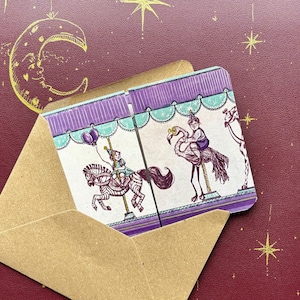 May include: A whimsical greeting card featuring a carousel design with a horse and a flamingo, in a brown envelope. The card has purple and teal accents, with a maroon background adorned with gold stars and a crescent moon.