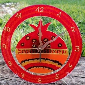 May include: A red glass clock featuring a pomegranate design. The clock face has gold numbers and hands. The pomegranate is painted with orange, yellow, and black details.