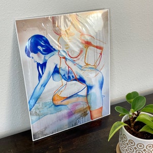 以下が含まれることがあります： 青、オレンジ、黄色の色合いで描かれた2つの図形の抽象画。図形は絡み合い、踊ったり抱き合ったりしているように見える。背景は薄いグレーで、ピンクと紫のヒントがある。