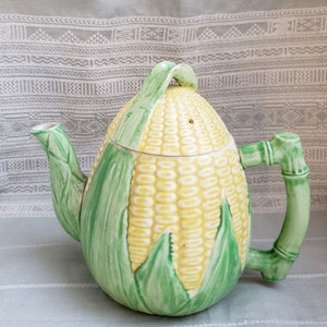 Peut inclure: Une théière en céramique en forme d'épi de maïs avec des feuilles vertes et une poignée en bambou. La théière est jaune et verte.