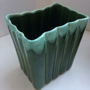 Peut inclure: Un pot en céramique vert avec un bord ondulé et des nervures verticales. Le pot a un glaçage vert clair sur le bord supérieur.