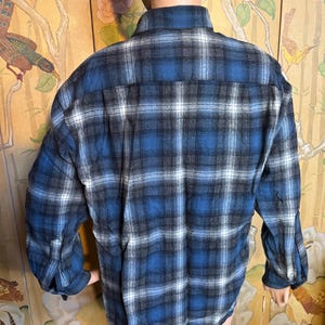 May include: A blue, black, and white checked flannel shirt. The shirt features long sleeves and a button-down front. The checked pattern is a classic design, suitable for casual wear. The shirt is made of a soft, comfortable material.