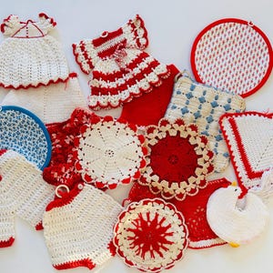 May include: A collection of assorted crochet items including dress-shaped, circular, and square potholders in red, white, and blue. The pieces feature intricate stitching, scalloped edges, and hanging loops, showcasing various geometric and floral patterns.